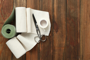 Medical bandage rolls, sticking plaster and scissors on wooden background, flat lay. Space for text