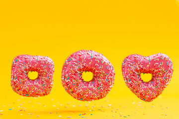 Three doughnuts of different shapes, with pink icing, on a yellow background. Copy space