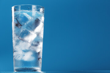 A glass with ice water and ice cubes on a blue background.