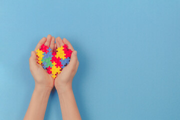 Kid hand holding colorful heart on light blue background. World autism awareness day concept