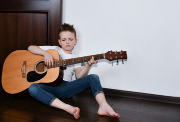 Sad boy sits at home on the floor and plays the guitar. 