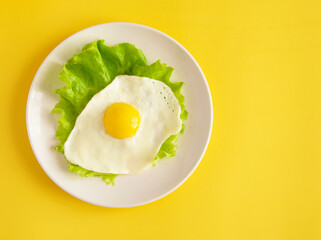 Fried eggs with lettuce on a white plate. View from above. Minimalistic composition on a yellow background.