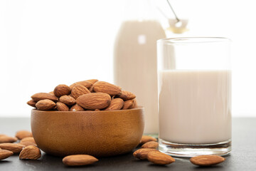 Almond milk with almond in a wooden bowl on black background. (selective focus; close-up shot)