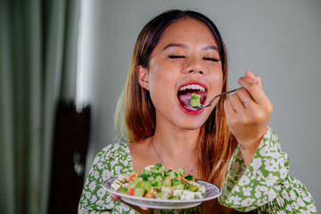 beautiful young asian woman eating healthy mediterranean food. smiling happy girl eating greek salad