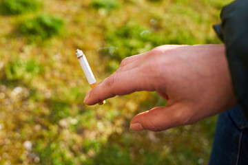 Mano sujetando un cigarrillo a medio uso sobre hierba verde