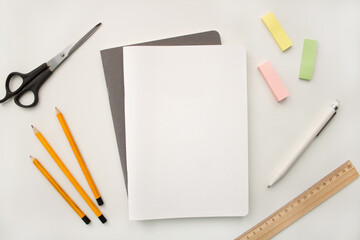 Notepad on a white background with colored pencils and felt-tip pens, rulers and scissors. The notebook lies on a plain background with space for writing. Composition of writing to-dos for the day.