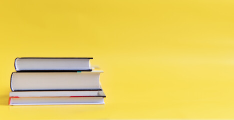 A stack of books on a yellow background. The books are on a plain background with space for writing. Composition of a reading person.