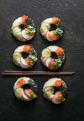Sushi donuts with salmon, cucumber and radish on dark background top view. Hybrid Foods.
