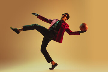 Fototapeta na wymiar High-fashion styled man in red jacket playing basketball isolted over brown background