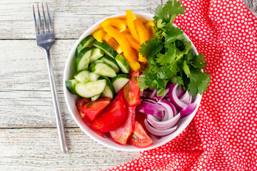 Plate of rainbow salad with different vegetables and herbs in white bowl on white wooden background