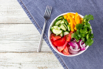 Plate of rainbow salad with different vegetables and herbs in white bowl on white wooden background