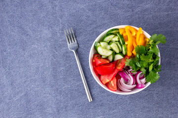 Plate of rainbow salad with different vegetables and herbs in white bowl on blue tablecloth