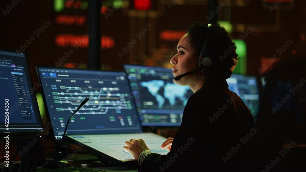 Poster Multiethnic Female IT Technical Support Specialist Talking with a Client in Headphones and Working on Desktop Computer in Monitoring Control Room with Big Digital Screens with Server Blockchain Data.