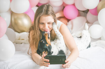 Lovely lady in pajama making selfie in her bedroom using phone and kiss her dog. Indoor portrait  girl with baloons in morning. Husband surprising his wife.