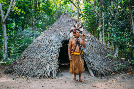 Shaman of the Patax&oacute; tribe, wearing feather headdress and smoking a pipe. Brazilian Indian looking at the right