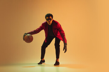 Fototapeta na wymiar High-fashion styled man in red jacket playing basketball isolted over brown background