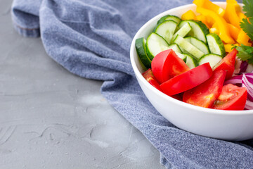 Plate of rainbow salad with different vegetables and herbs in white bowl on grey stone background