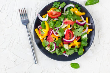 Plate of rainbow salad with different vegetables and herbs on black plate on white stone background