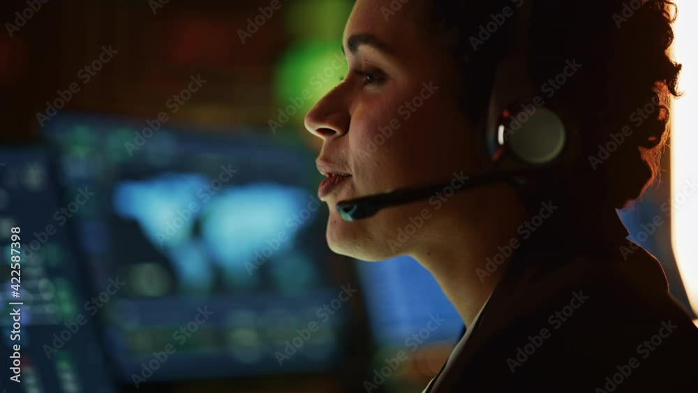 Poster Close Up Portrait of Multiethnic Female IT Technical Support Specialist Talking with a Client in Headphones and Working on Desktop Computer in Monitoring Control Room with Big Digital Screens.