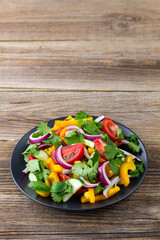 Plate of rainbow salad with different vegetables and herbs on black plate on wooden background