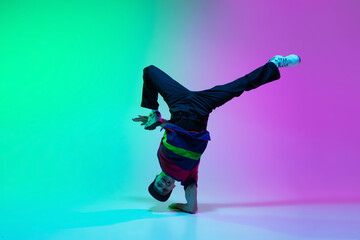 Beautiful sportive boy dancing hip-hop in stylish clothes on colorful gradient background at dance...