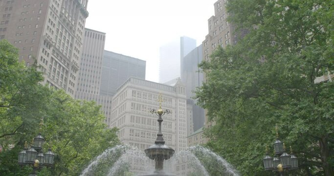 A beautiful water fountain in a green city park surrounded by tall buildings