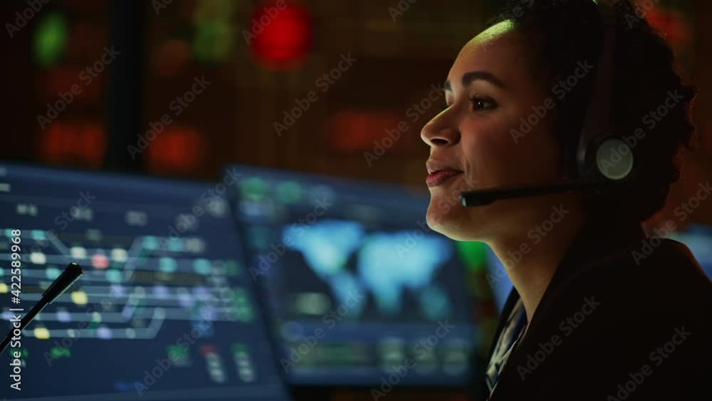 Poster Close Up Portrait of Multiethnic Female IT Technical Support Specialist Talking with a Client in Headphones and Working on Desktop Computer in Monitoring Control Room with Big Digital Screens.