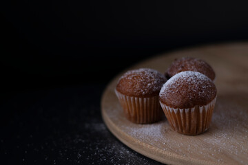 three muffins covered in powdered sugar on wooden stand isolated on black dark background. sweet bakery