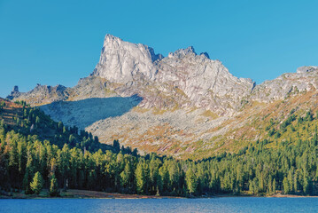 View of the Zvezdny peak behind the lake Lake Svetloye in Ergaki on an autumn morning with blue sky and trees 