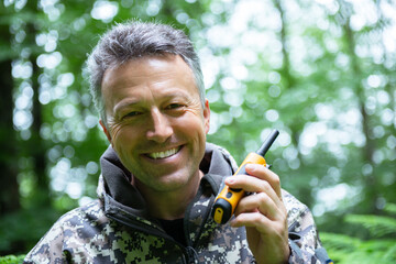 Smiling mature man walking and hiking in mountain forest and using radio set. Male spring outdoor portrait.