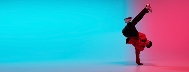 Beautiful sportive boy dancing hip-hop in stylish clothes on colorful gradient background at dance...