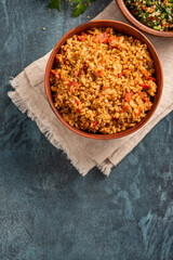 Easy bulgur pilaf (pilavi) with tomatoes in a ceramic bowl on a dark background top view. Turkish cuisine, vegan food. Copy space for text