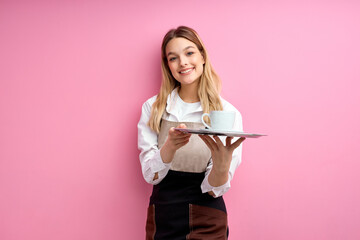 Pretty female waiter offering cup of coffee isolated on pink background