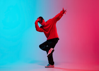 Beautiful sportive boy dancing hip-hop in stylish clothes on colorful gradient background at dance...