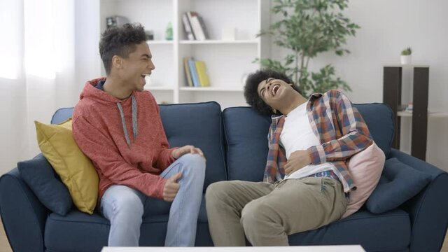Cheerful mixed-race boys joking and laughing together, sitting on couch, fun
