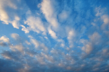 Blue sky background, white fluffy clouds lit by sunset light.