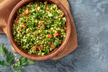 Traditional Arabic salad tabbouleh in a wooden bowl on a dark background top view. Arabic cuisine,...