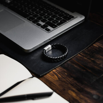 Laptop On A Leather Desk Mat, Leather Bracelet And Notebook On Wooden Table