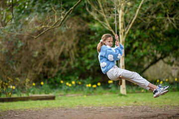 Fototapeta premium Girl on a stick swing.A young girl smiling while swinging on a stick swing at a park.