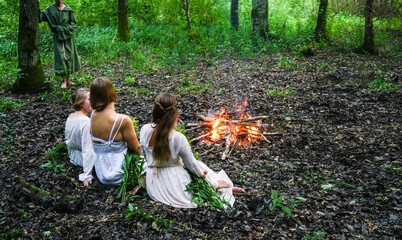 three beautiful witches looking at the fire in dark forest. magician woman wear white long dress. ...