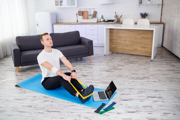 Online training. Young man doing exercise with fitness rubber bands with online tutorial at home, free space. Doing sports at home