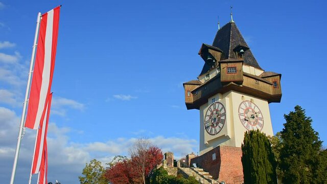 The famous clock tower on Schlossberg hill, one of the city of Graz attractions and the national flag of Austria waving in the wind, in Styria region, Austria
