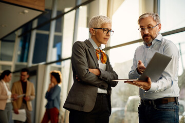 Female CEO talking to businessman who is showing her data on laptop during a briefing in the office.