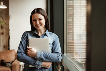 happy freelancer holding laptop while standing near window