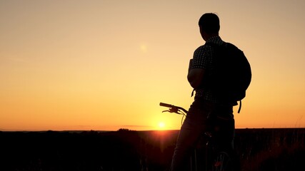 Fototapeta na wymiar Tourist a healthy young man rides a Bicycle to edge of hill, enjoying nature and sun. A free traveler travels with a bicycle at sunset. concept of adventure and travel. lonely cyclist resting in park.
