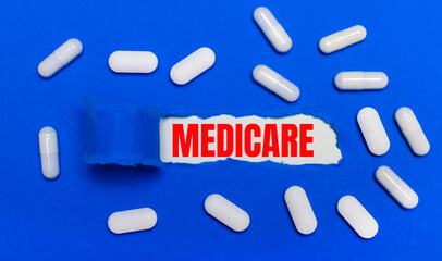 White pills lie on a beautiful blue background. In the center is white paper with the inscription MEDICARE. Medical concept. View from above.