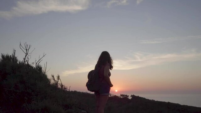 Woman with a backpack in a mountain watching the sunset in the sea.
