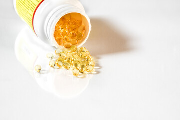 Vitamin D3 clear yellow gel capsules spilling from supplement bottle.  White background with reflection and copy space