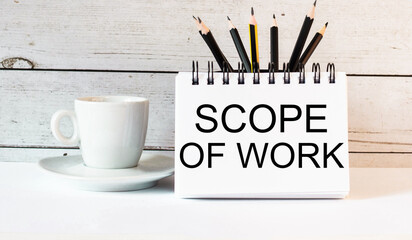 The words SCOPE OF WORK is written in a white notepad near a white cup of coffee on a light background