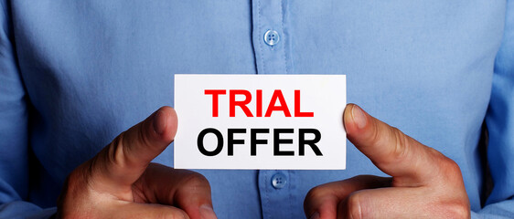 The words TRIAL OFFER is written on a white business card in a man's hands. Business concept